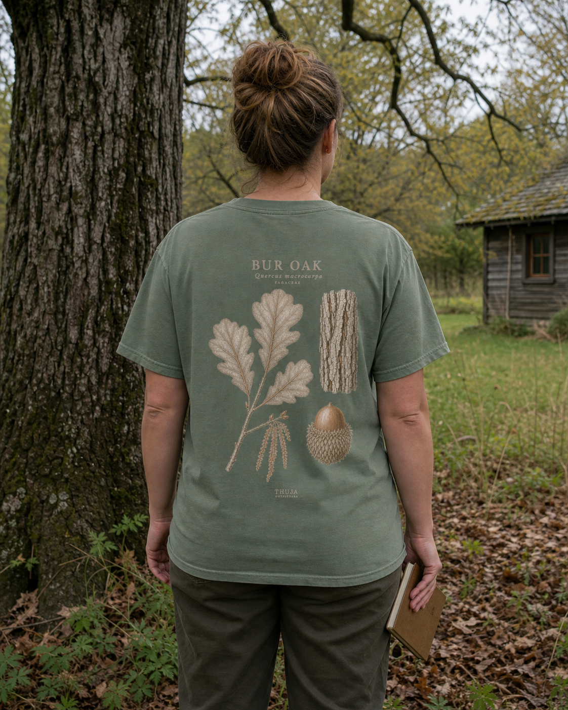 Woman wearing the Moss Bur Oak Botanical T-Shirt beside a Northwoods cabin, back view
