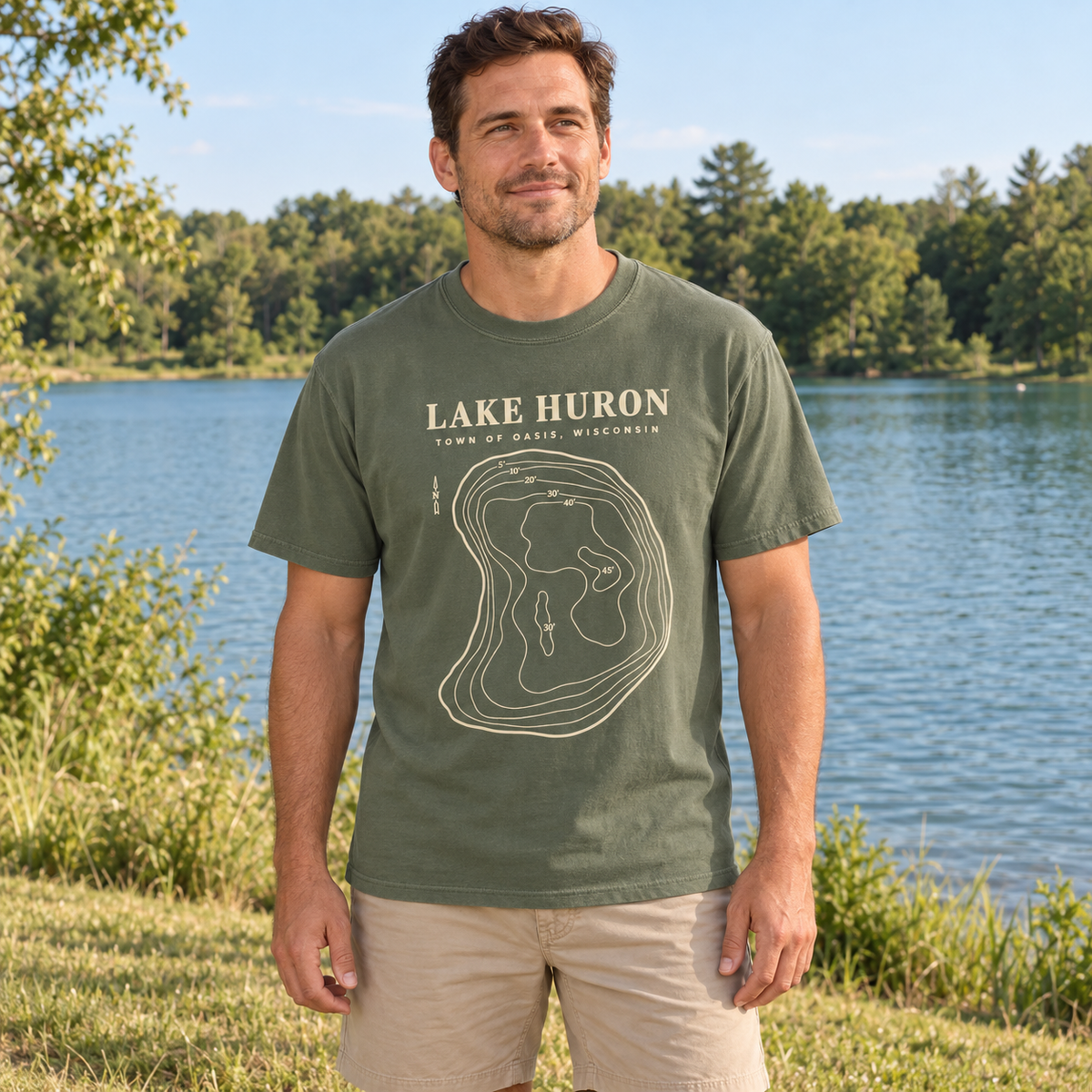 Adult Moss — lakeshore lifestyle mockup of the Lake Huron Field Survey T-shirt with cream contour-map artwork and Town of Oasis, Wisconsin lettering, in a generated wooded lakeside setting.