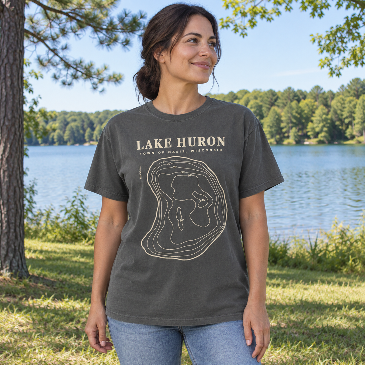 Adult Pepper — park lifestyle mockup of the Lake Huron Field Survey T-shirt with cream contour-map artwork and Town of Oasis, Wisconsin lettering, in a generated wooded lakeside setting.