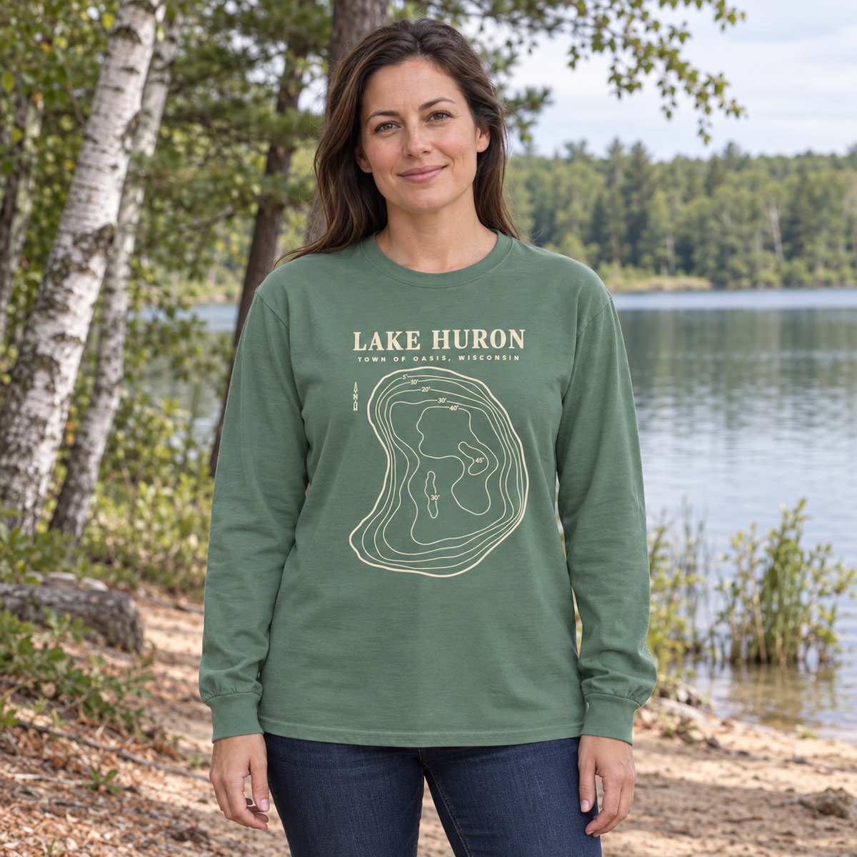 Light Green Comfort Colors 6014 adult Lake Huron long-sleeve shirt with cream contour artwork and Town of Oasis, Wisconsin lettering, worn by an adult beside a small Wisconsin lake in a generated lifestyle scene.