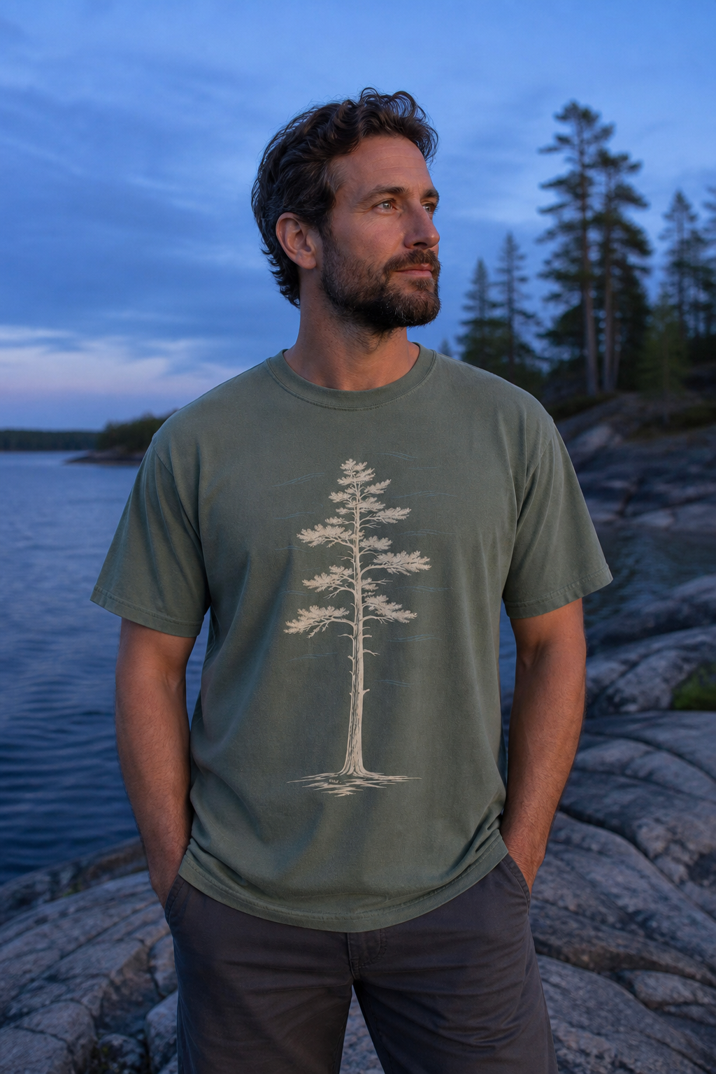 Person wearing the Moss White Pine Stand Comfort Colors T-Shirt on a rocky Northwoods lakeshore